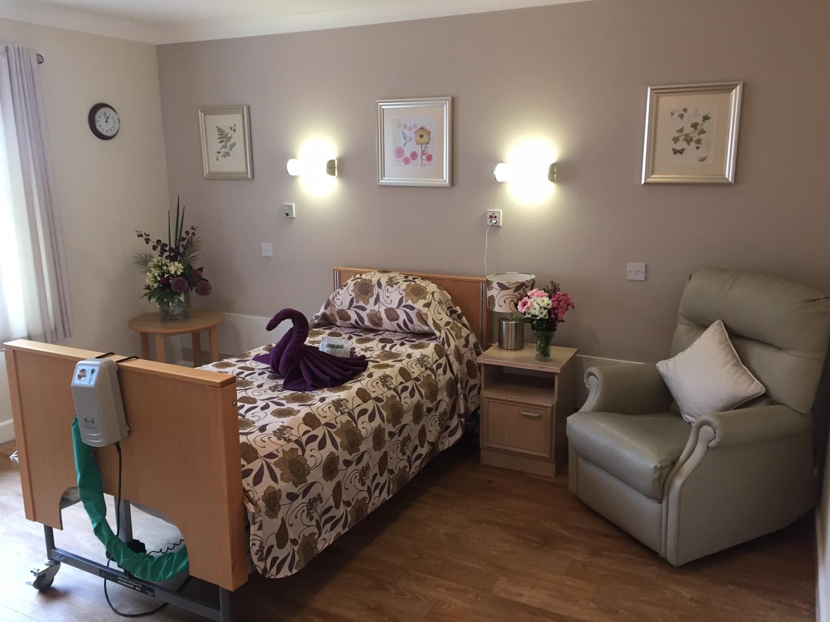 nursing home bedroom with profiling bed, floral sheets and armchair